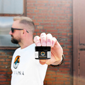 Mats mit einem Glas AYUVANA Shilajit in der Hand